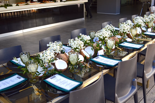 Table setting with elegant flower arrangements and coconut halves, each seat showcasing the menu